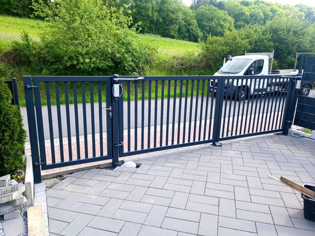 Anthrazitfarbenes Drehtor mit Antriebsarm an einer gepflasterten Einfahrt
