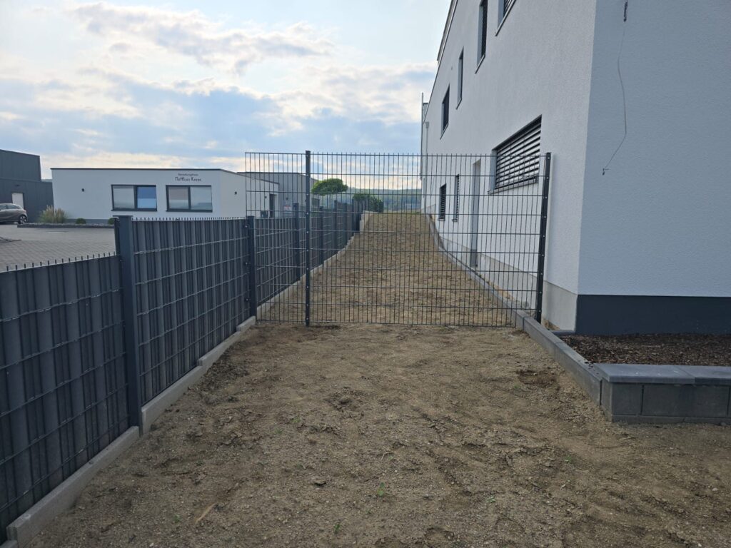 Doppelstabzaun mit anthrazitfarbenen Sichtschutzstreifen zwischen zwei Gebäuden
