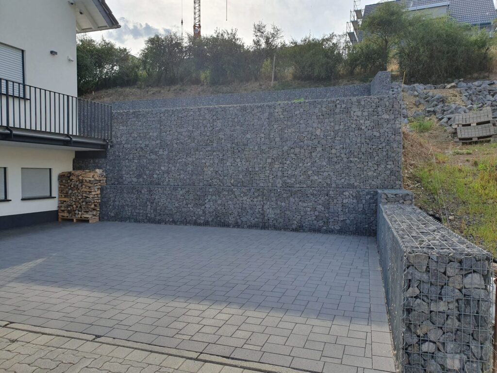 Gabionen als Stützmauer am Hang hinter einem Wohnhaus