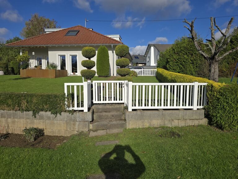 Weißer Gartenzaun auf einer Stützmauer vor einem Bungalow