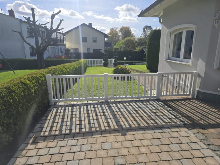 Weißer Zaun als Abgrenzung einer gepflasterten Terrasse