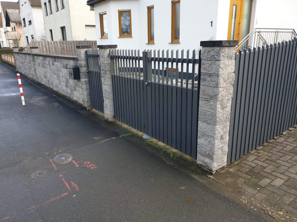 Anthrazitfarbener Lattenzaun auf einer Natursteinmauer an der Straße