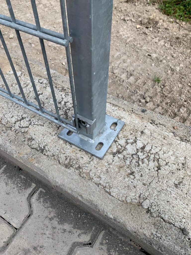 Verzinkter Zaunpfosten mit Fußplatte auf einem Betonstreifen