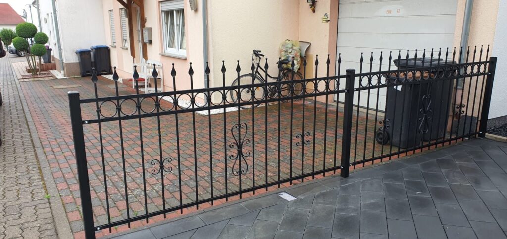 Schwarzer schmiedeeiserner Zaun mit Ornamenten an einer Hofeinfahrt