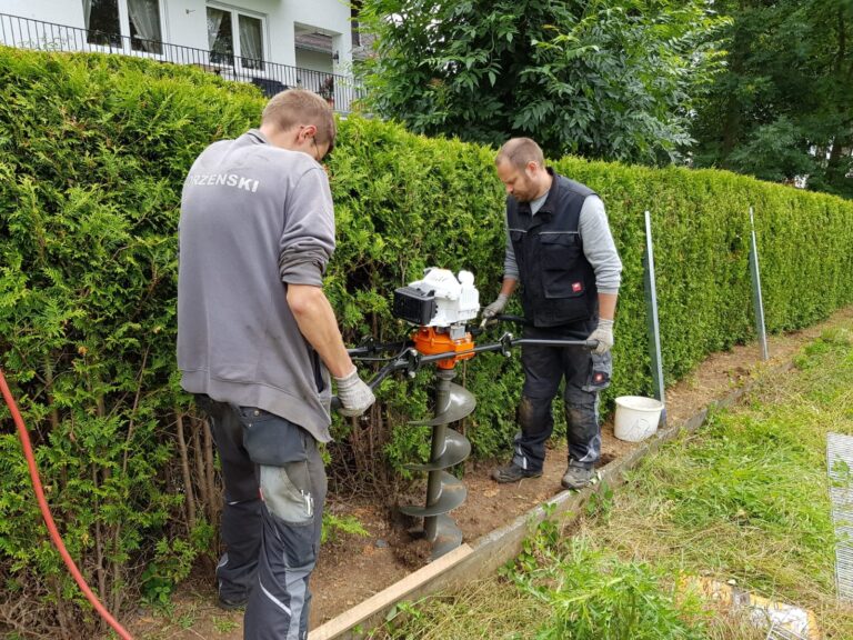 Zwei Monteure setzen mit einem Erdbohrer Löcher für Zaunpfosten